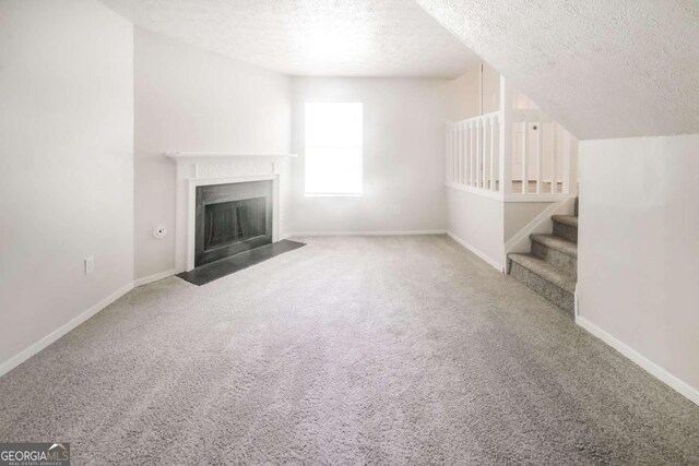 unfurnished living room featuring stairway, baseboards, a fireplace with flush hearth, a textured ceiling, and carpet flooring