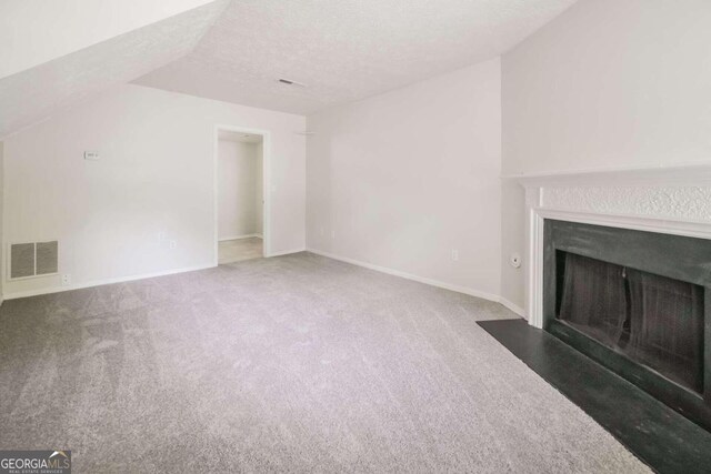 unfurnished living room featuring carpet flooring, visible vents, a fireplace with flush hearth, and a textured ceiling