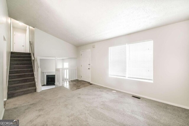 unfurnished living room featuring a fireplace with flush hearth, carpet, visible vents, and a textured ceiling