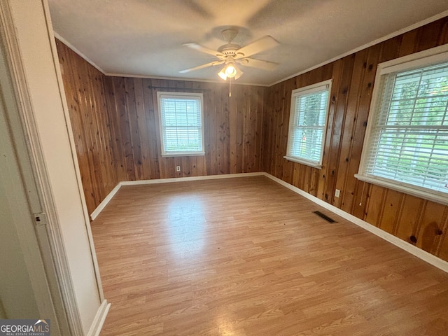 spare room with light wood-type flooring, crown molding, wood walls, and ceiling fan