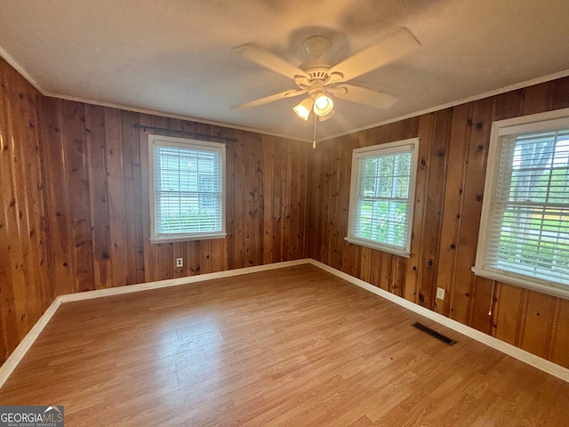 spare room featuring light wood-type flooring, ceiling fan, a wealth of natural light, and wooden walls