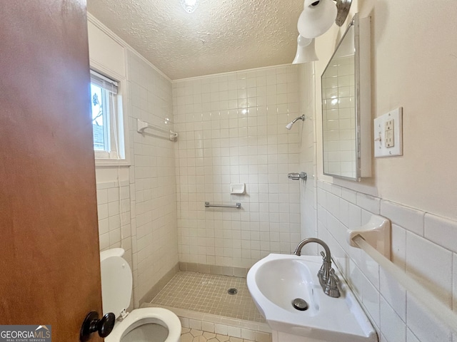 bathroom with tile patterned floors, toilet, tile walls, tiled shower, and a textured ceiling