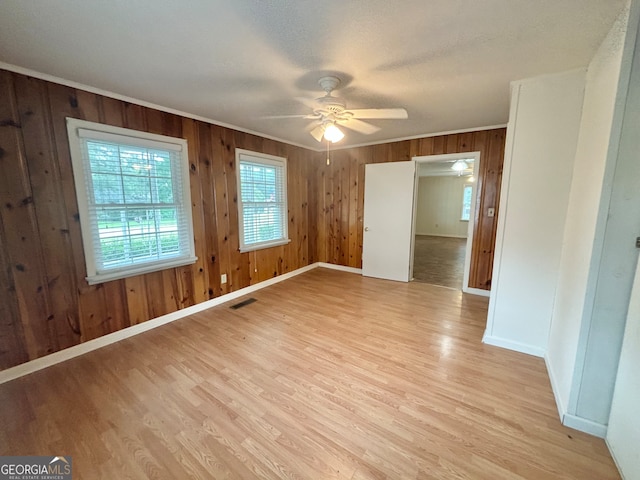 empty room with light wood-type flooring, ceiling fan, and wooden walls