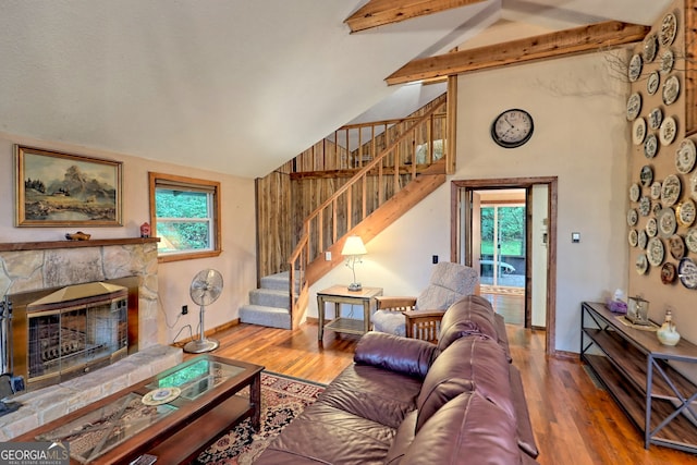 living room with high vaulted ceiling, hardwood / wood-style flooring, beamed ceiling, and a stone fireplace