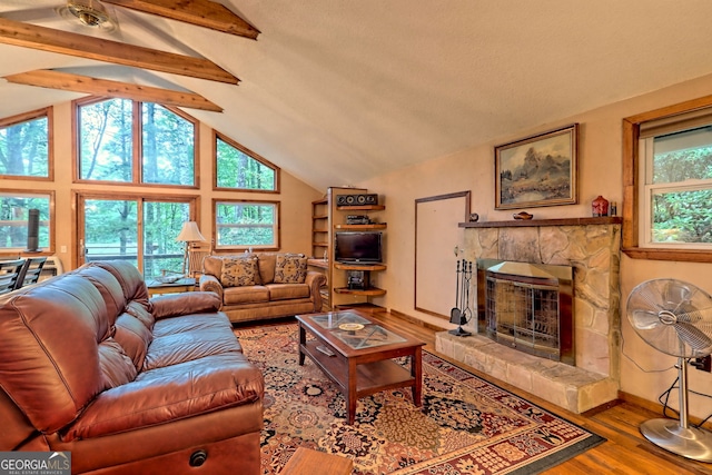 living room featuring a healthy amount of sunlight, wood-type flooring, vaulted ceiling with beams, and a stone fireplace