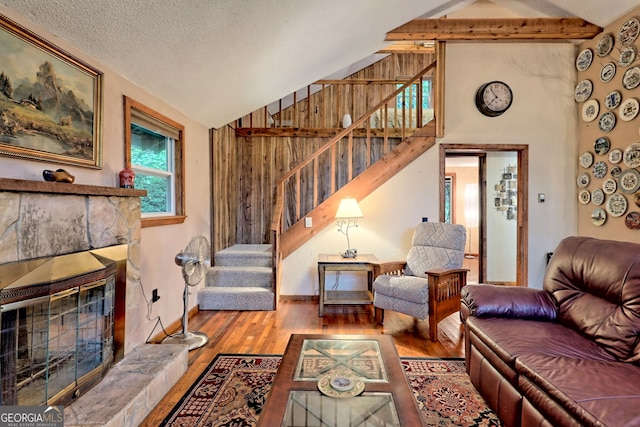 living room with lofted ceiling with beams, a textured ceiling, hardwood / wood-style floors, and a stone fireplace