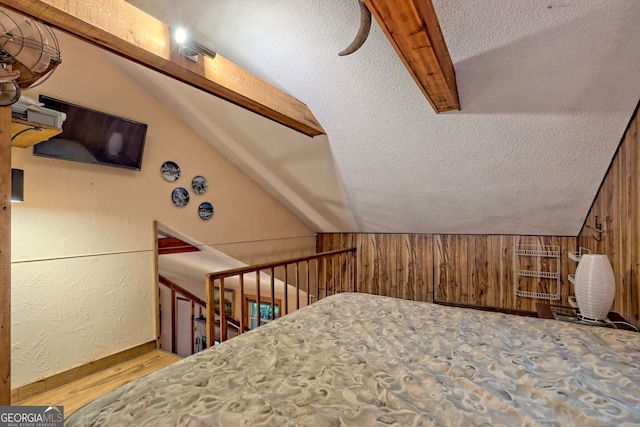 bedroom with light wood-type flooring, a textured ceiling, wood walls, and lofted ceiling