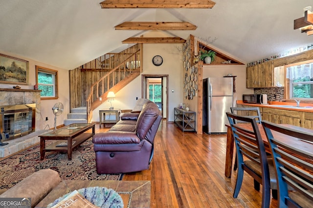 living room featuring beamed ceiling, a textured ceiling, wood-type flooring, sink, and a stone fireplace