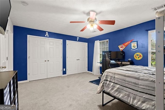 carpeted bedroom featuring a textured ceiling, ceiling fan, and multiple closets