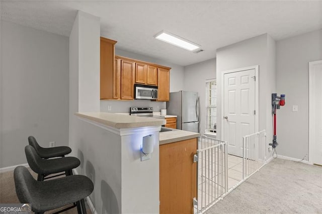 kitchen featuring light colored carpet, appliances with stainless steel finishes, kitchen peninsula, and a kitchen breakfast bar