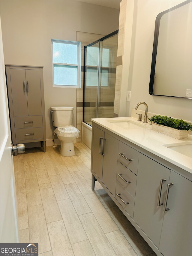 full bathroom with hardwood / wood-style flooring, shower / bath combination with glass door, vanity, and toilet