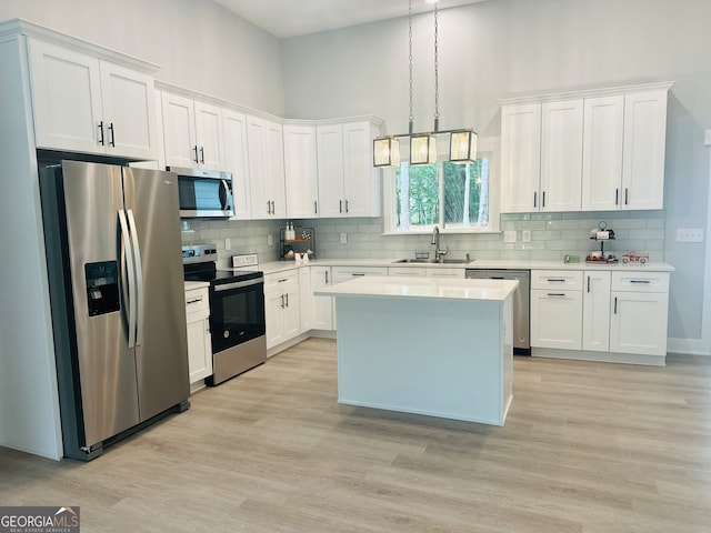 kitchen featuring pendant lighting, sink, white cabinets, light hardwood / wood-style flooring, and stainless steel appliances