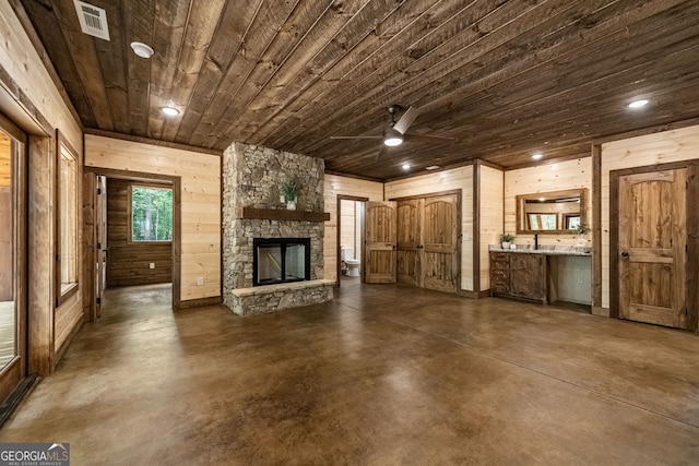 unfurnished living room featuring a stone fireplace, wooden walls, ceiling fan, and wood ceiling