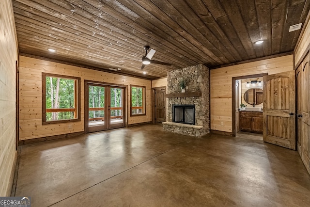 unfurnished living room with french doors, wood ceiling, ceiling fan, wooden walls, and a stone fireplace