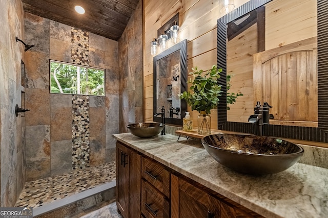 bathroom featuring wooden walls, vanity, vaulted ceiling, and tiled shower