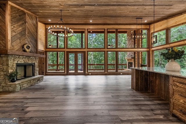 unfurnished living room featuring an inviting chandelier, a stone fireplace, dark hardwood / wood-style floors, and wood ceiling