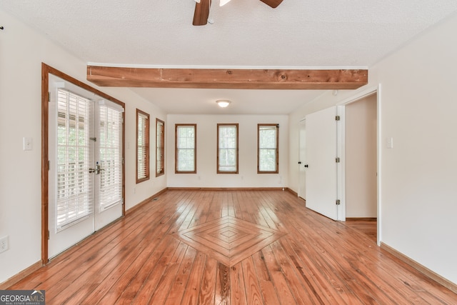 empty room featuring a wealth of natural light, beamed ceiling, french doors, and a textured ceiling