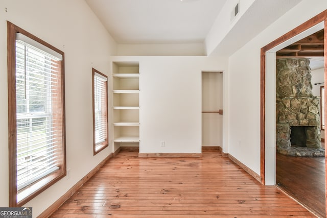 unfurnished room with built in features, light hardwood / wood-style flooring, and a fireplace