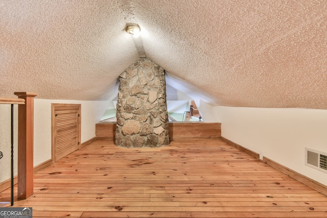 additional living space with a textured ceiling, light wood-type flooring, and lofted ceiling