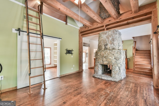 living room with a barn door, wood-type flooring, a stone fireplace, ceiling fan, and beam ceiling