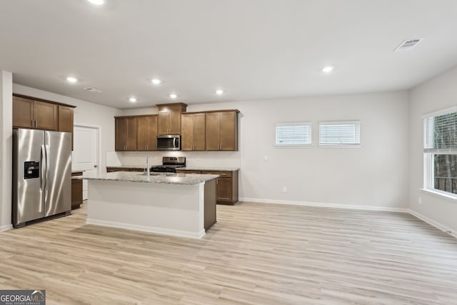 kitchen featuring light stone countertops, appliances with stainless steel finishes, sink, light hardwood / wood-style flooring, and an island with sink