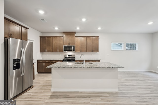 kitchen with light stone countertops, decorative backsplash, stainless steel appliances, sink, and a center island with sink