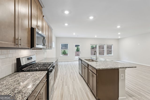 kitchen featuring light stone countertops, tasteful backsplash, stainless steel appliances, sink, and a center island with sink