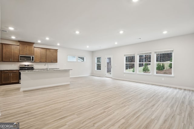 kitchen featuring backsplash, a kitchen island with sink, sink, light wood-type flooring, and appliances with stainless steel finishes