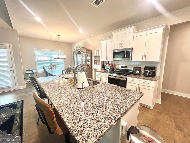 kitchen with a center island with sink, a notable chandelier, appliances with stainless steel finishes, sink, and white cabinetry