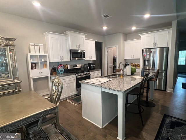 kitchen featuring stone counters, stainless steel appliances, sink, dark hardwood / wood-style floors, and a kitchen island with sink