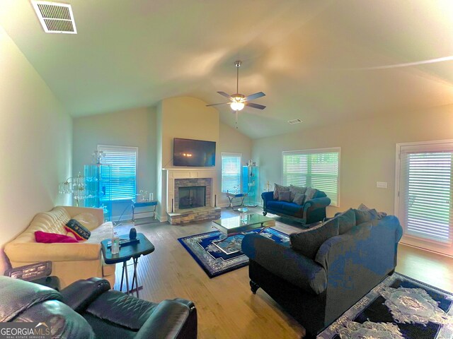 living room with light hardwood / wood-style flooring, ceiling fan, a stone fireplace, and vaulted ceiling