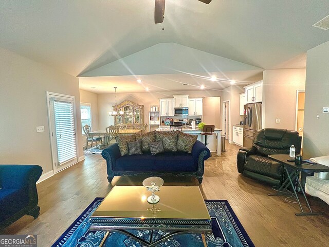 living room featuring ceiling fan with notable chandelier, vaulted ceiling, and light hardwood / wood-style floors