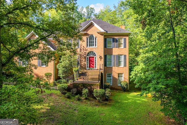 view of front of house with a front yard, brick siding, and a chimney