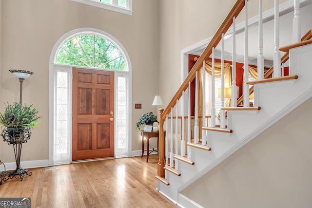 foyer entrance with a towering ceiling, visible vents, wood finished floors, stairs, and baseboards