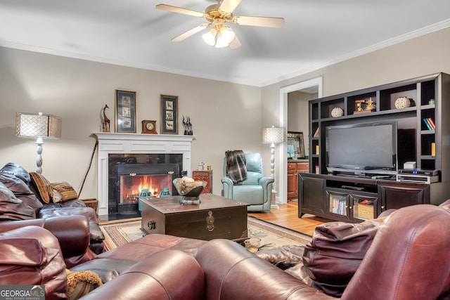 living area featuring ornamental molding, light wood-type flooring, a fireplace, and a ceiling fan