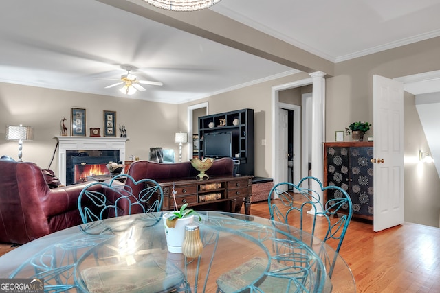 dining room featuring ornamental molding, a ceiling fan, ornate columns, wood finished floors, and a glass covered fireplace