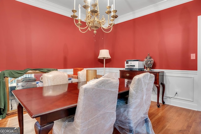 dining space featuring a notable chandelier, a decorative wall, crown molding, wood finished floors, and a wainscoted wall