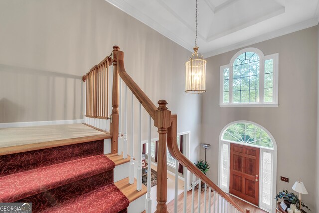 foyer with crown molding, a tray ceiling, stairway, and a chandelier