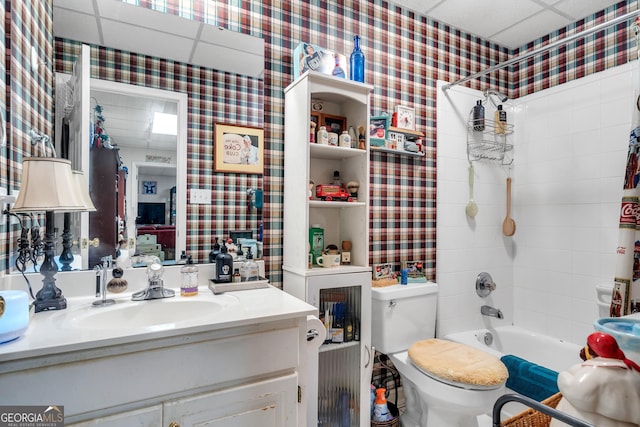 bathroom featuring a paneled ceiling, vanity, toilet, shower / tub combo with curtain, and wallpapered walls
