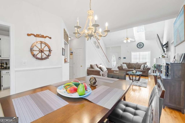 dining area featuring ceiling fan with notable chandelier, vaulted ceiling, and light hardwood / wood-style floors