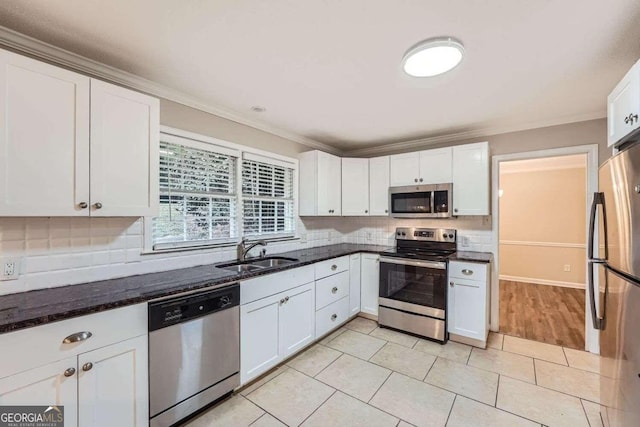 kitchen with dark stone counters, ornamental molding, stainless steel appliances, sink, and white cabinets