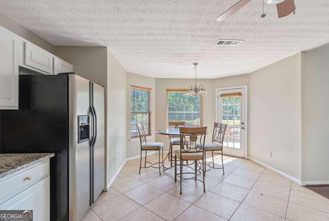 tiled dining space featuring ceiling fan with notable chandelier and a textured ceiling