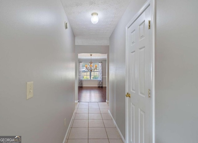 corridor featuring a chandelier, a textured ceiling, and light tile patterned floors