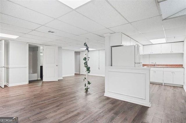 basement featuring white fridge, dark wood-type flooring, a paneled ceiling, and sink