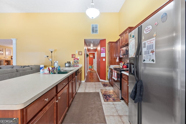 kitchen with decorative light fixtures, light tile patterned floors, an island with sink, sink, and appliances with stainless steel finishes