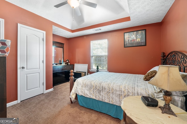 bedroom with a textured ceiling, carpet, ceiling fan, and a tray ceiling