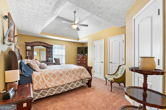 carpeted bedroom featuring multiple closets, a raised ceiling, a textured ceiling, and ceiling fan