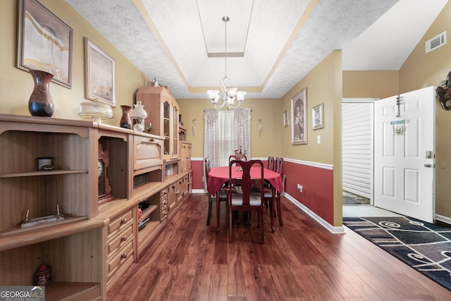 dining area featuring a tray ceiling, dark hardwood / wood-style floors, a chandelier, and a textured ceiling