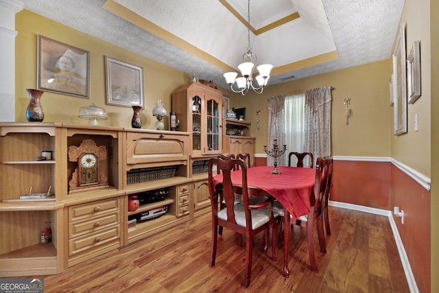 dining room featuring a textured ceiling, a raised ceiling, an inviting chandelier, ornamental molding, and hardwood / wood-style flooring