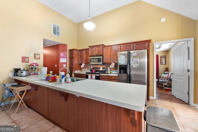 kitchen featuring decorative light fixtures, light tile patterned floors, appliances with stainless steel finishes, kitchen peninsula, and high vaulted ceiling